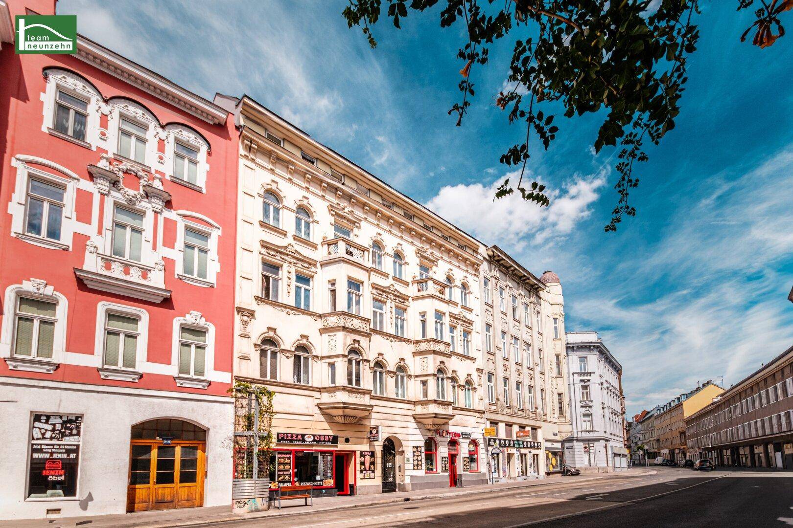 Belebte Straße mit historischen Gebäudefassaden und Geschäften unter blauem Himmel.