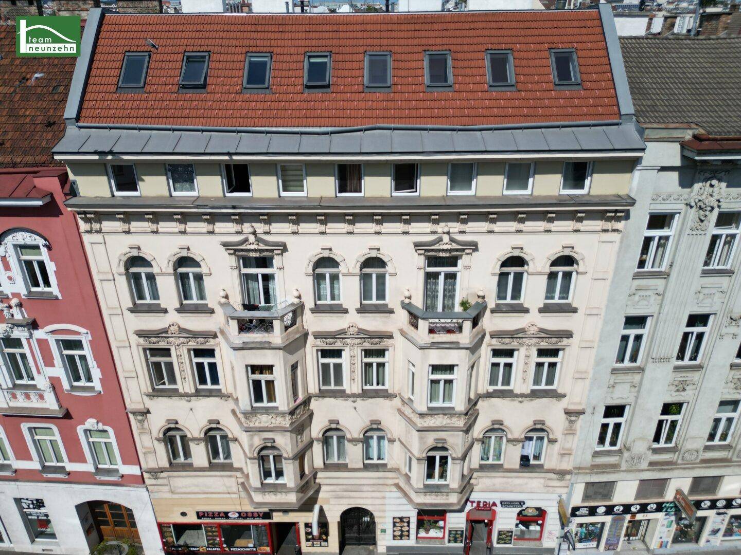 Historische Fassade eines Altbaus mit vielen Fenstern und einem roten Ziegeldach.