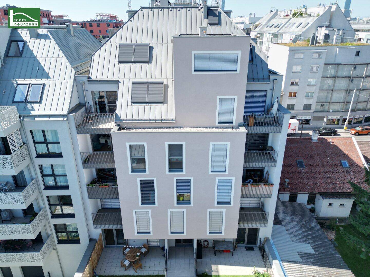 Moderne Wohnhausfassade mit Balkonen und Terrassen im Erdgeschoss, umgeben von städtischer Bebauung.