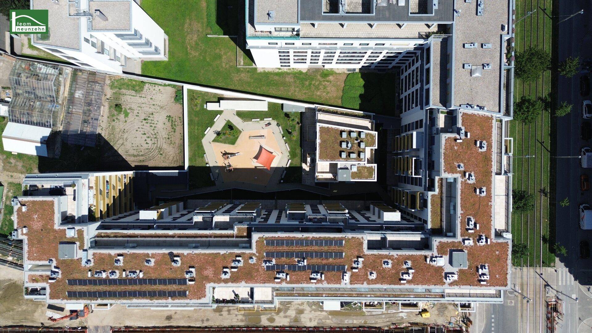 Vogelperspektive eines Wohnkomplexes mit Solaranlagen auf den Dächern und Innenhof.