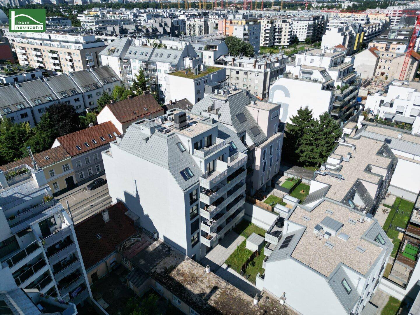 Luftaufnahme eines modernen Wohnkomplexes in städtischer Umgebung mit Grünflächen und umliegenden Gebäuden.