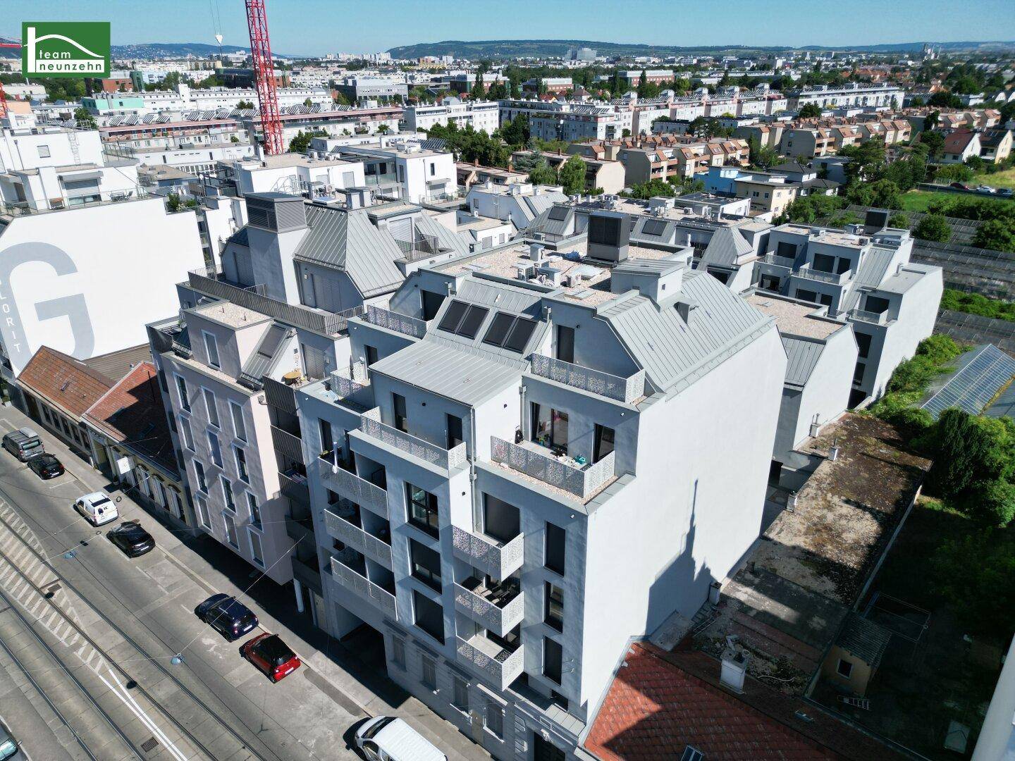Moderne Wohnanlage mit mehreren Gebäuden, Balkonen und Dachterrassen in städtischer Umgebung, umgeben von Grünflächen.
