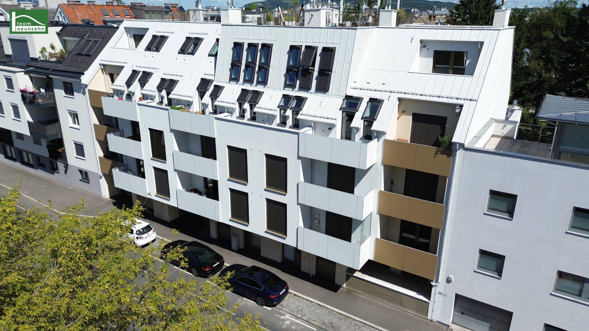 Moderne Wohnanlage mit weißer Fassade, Balkonen und Dachfenstern an einer städtischen Straße.