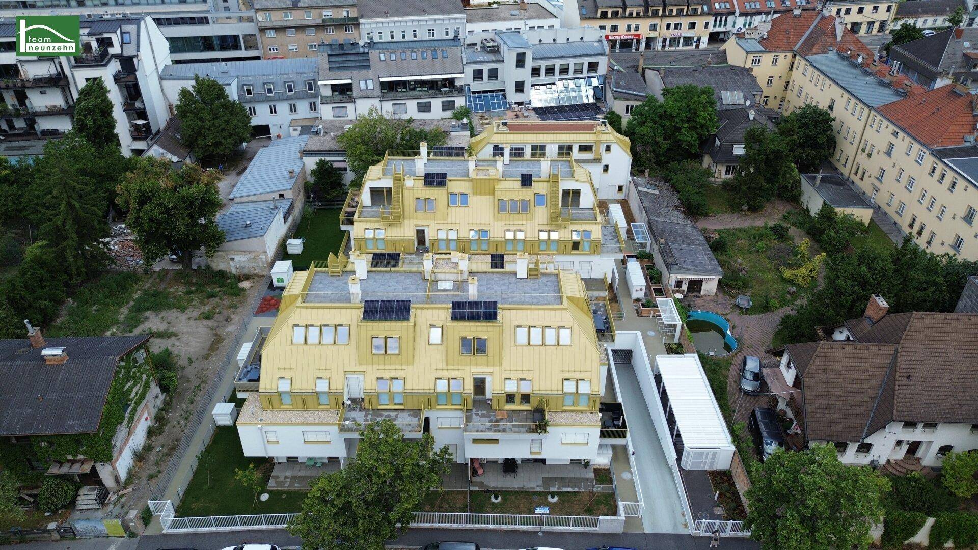 Weitläufige Luftansicht des Wohnkomplexes mit goldfarbenen Dächern, Solaranlagen und städtischer Umgebung.