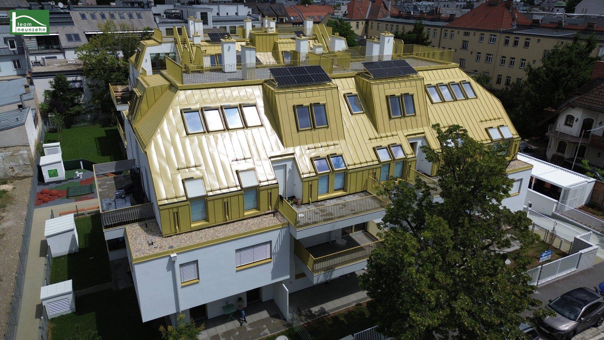 Moderne Wohnanlage mit goldfarbenem Mansarddach und Photovoltaikanlage in städtischer Umgebung.