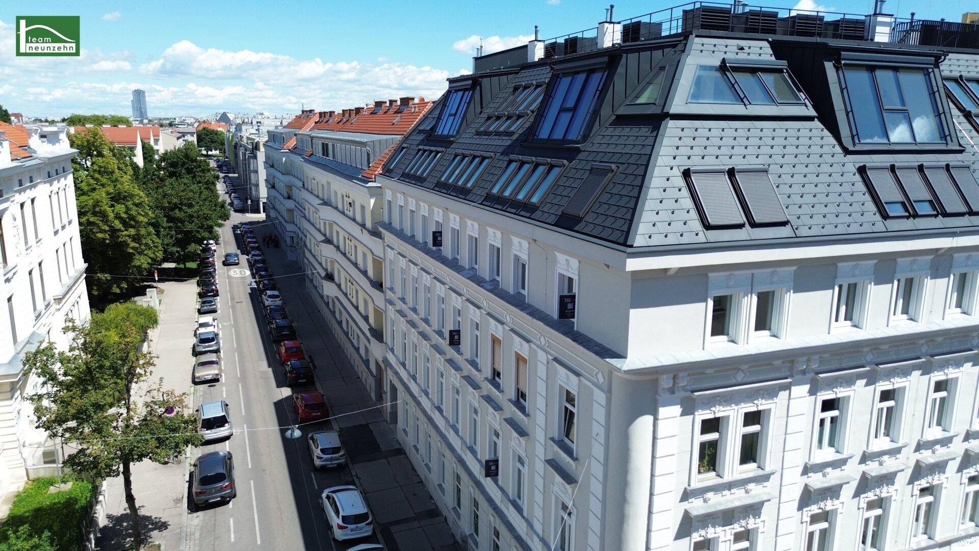 Luftaufnahme des Gebäudes und der umliegenden Straße mit parkenden Autos unter blauem Himmel.