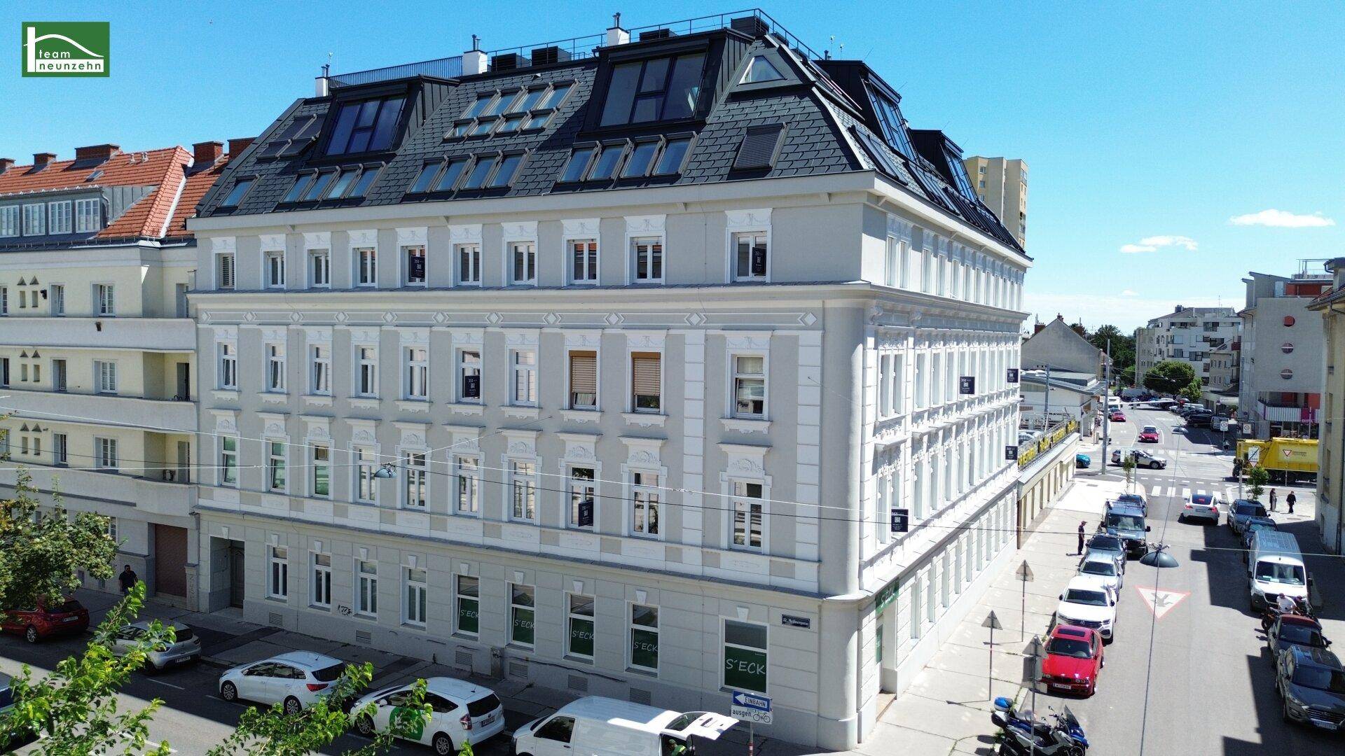 Weitläufige Ansicht des Eckgebäudes mit modernem Dachgeschoss und der belebten Straße.