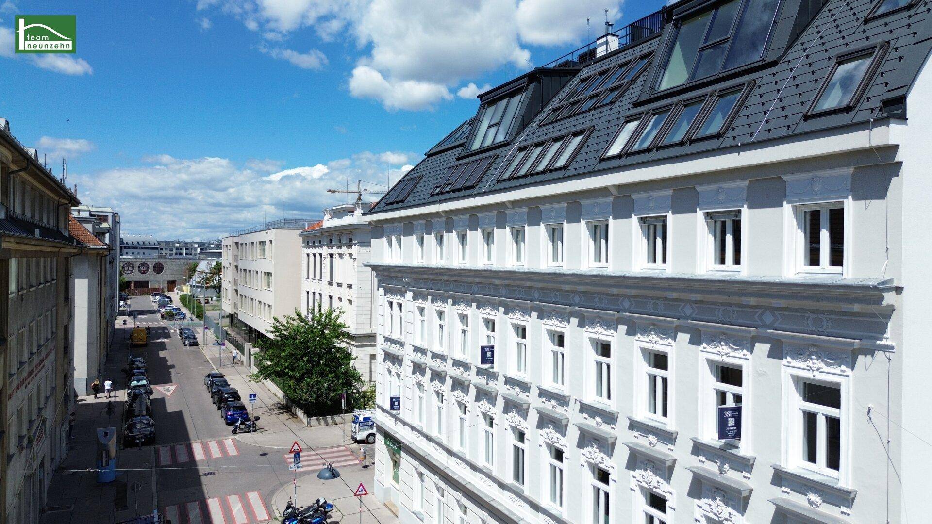 Seitenansicht des Gebäudes mit eleganter Fassade, vielen Fenstern und Blick auf die belebte Straße.