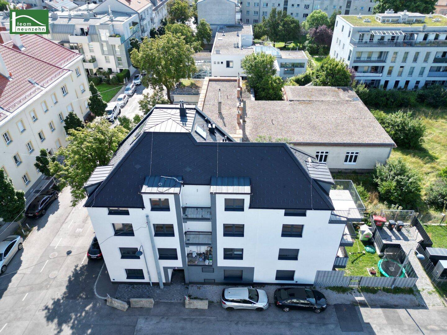 Luftaufnahme eines modernen Wohngebäudes mit dunklem Dach und umliegender Stadtlandschaft.
