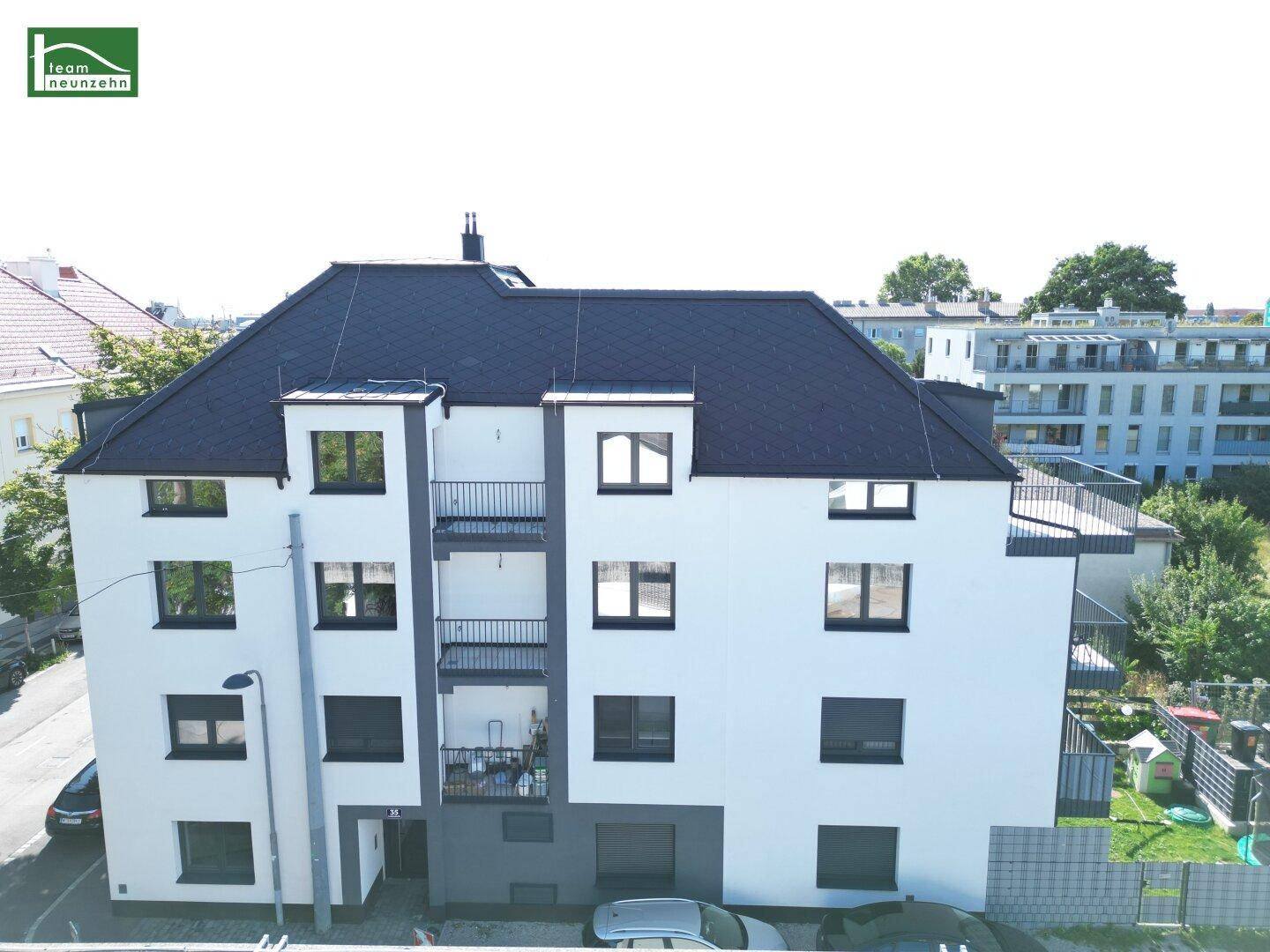 Modernes Mehrfamilienhaus mit dunklem Dach und Balkonen in städtischer Umgebung.