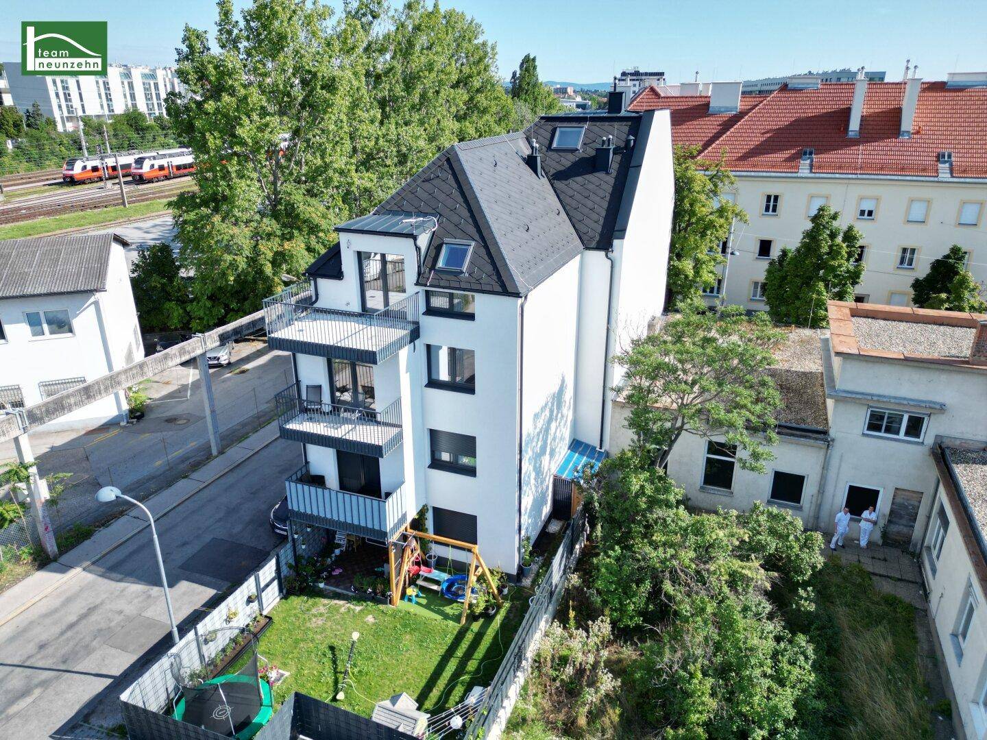 Modernes Gebäude mit Garten, Spielplatz und Balkonen in grüner Umgebung.