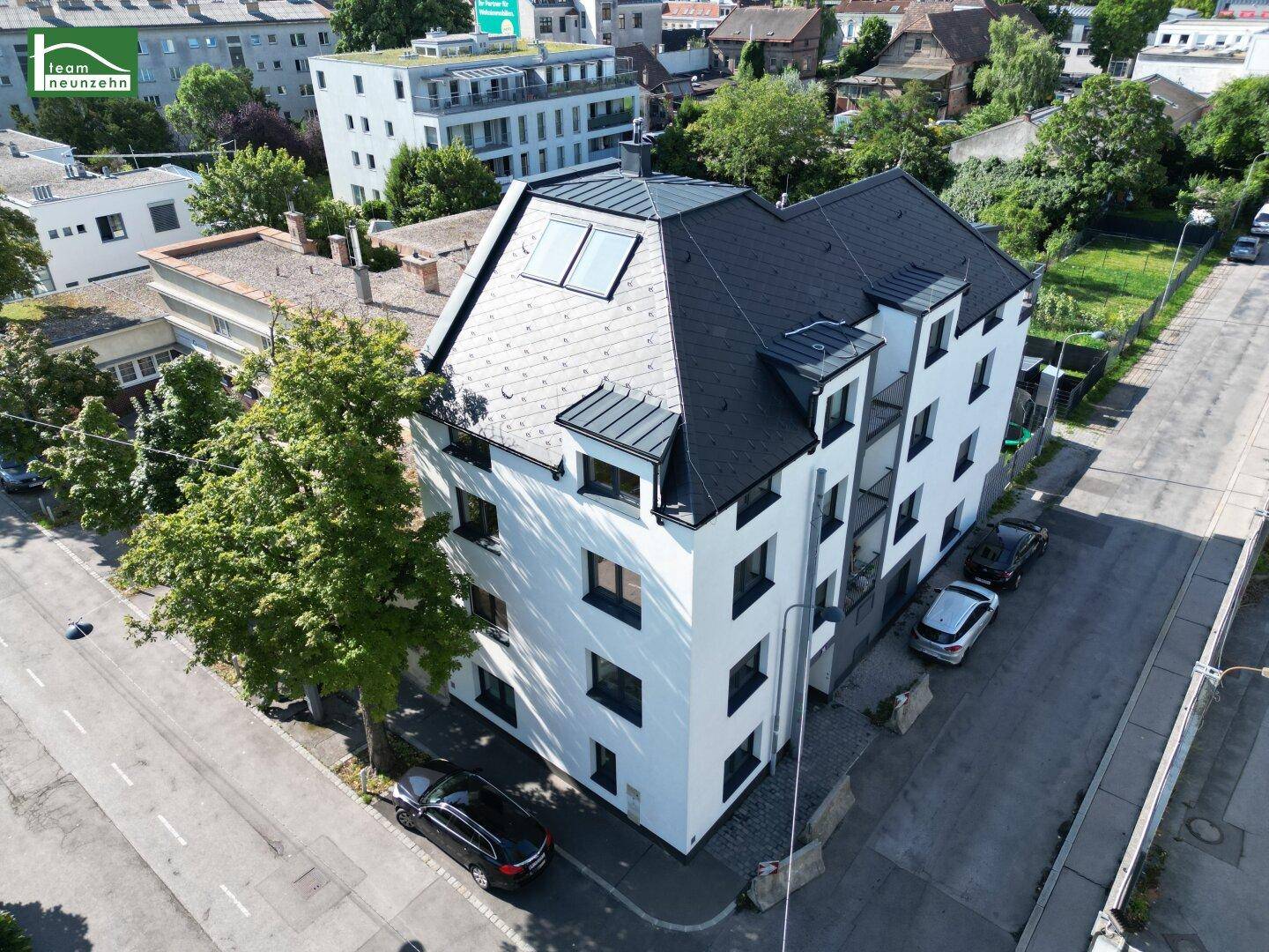 Luftaufnahme eines modernen Wohngebäudes mit dunklem Dach und weißer Fassade in städtischer Umgebung.