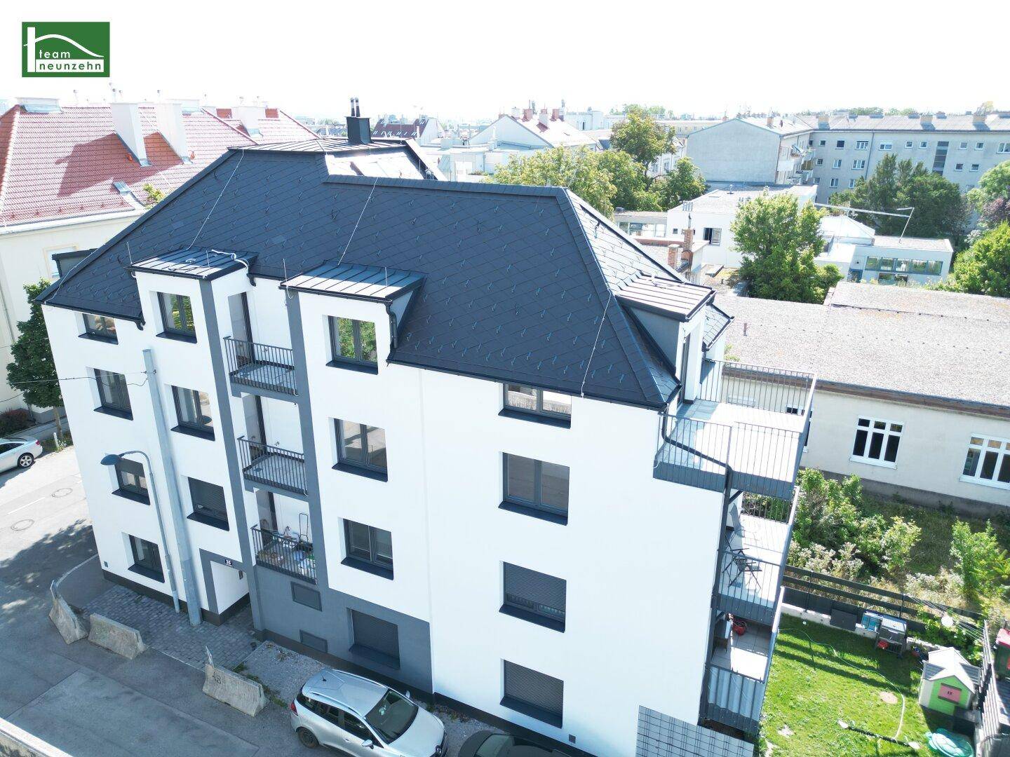 Luftaufnahme des modernen Wohngebäudes mit Balkonen und dunklem Dach in urbaner Umgebung.
