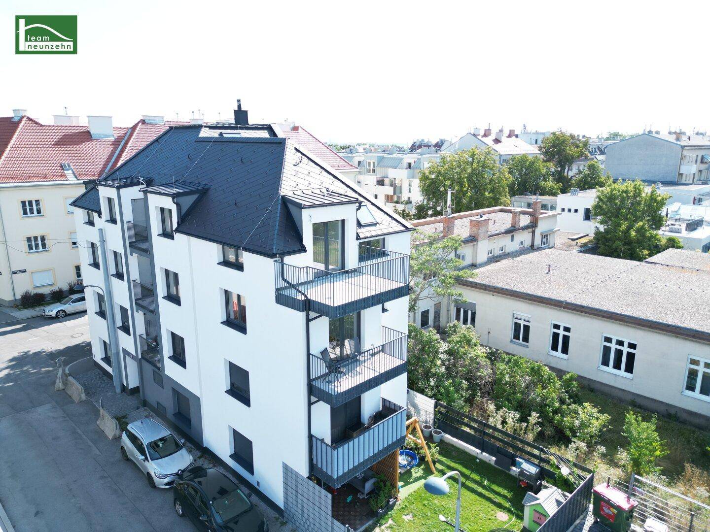 Luftaufnahme des modernen Wohngebäudes mit Balkonen und Dachterrasse, umgeben von städtischer Bebauung.