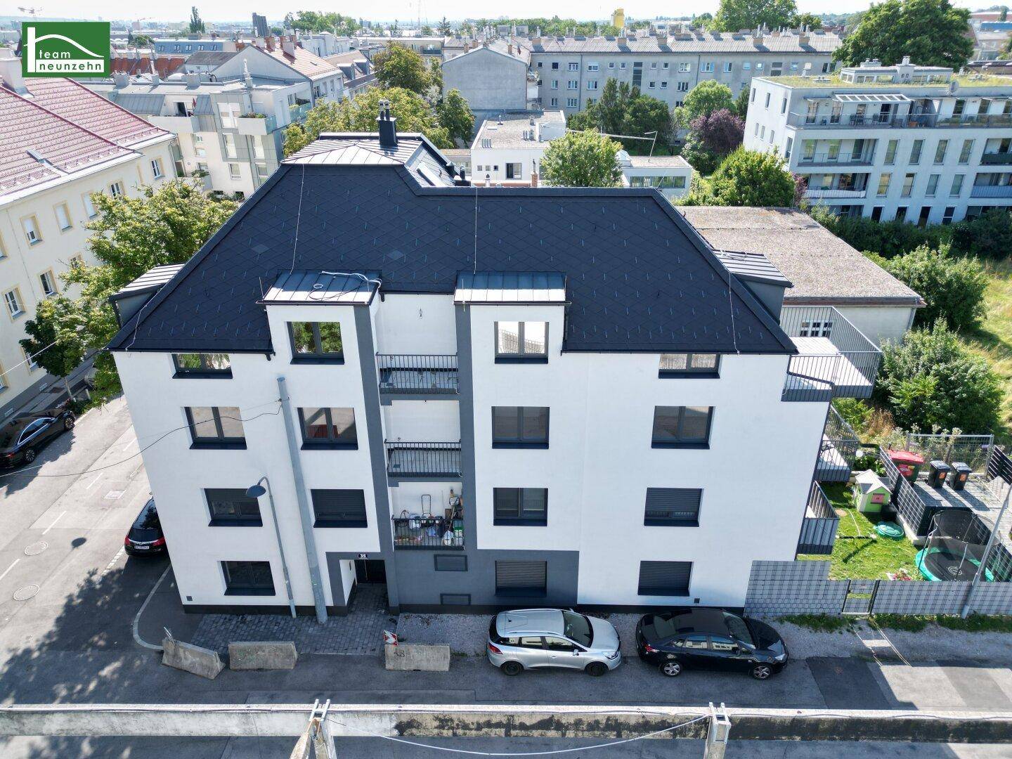 Vogelperspektive des Neubaus mit dunklem Dach und weißer Fassade, integriert in die städtische Umgebung.