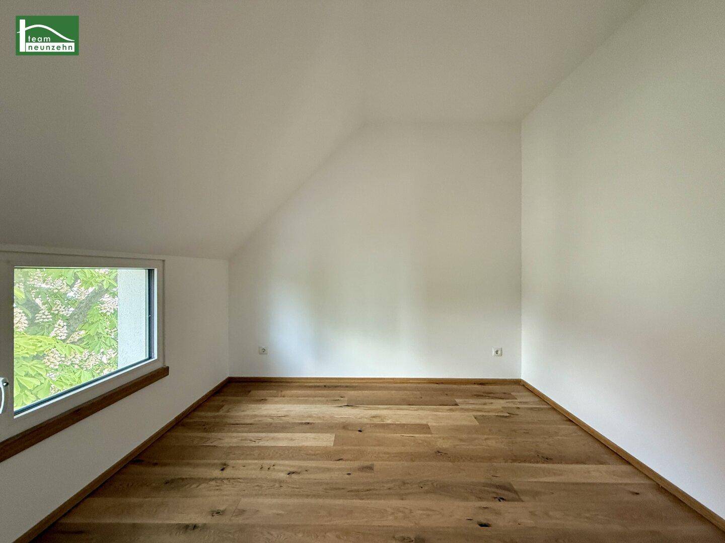 Heller Raum im Dachgeschoss mit Holzboden und einem Fenster, das viel Tageslicht hereinlässt.
