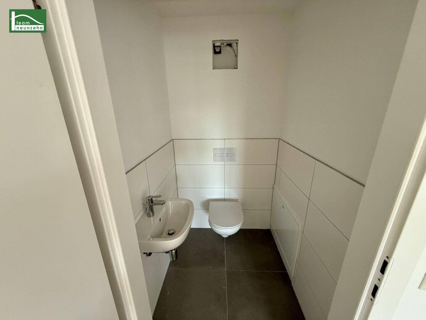 Kleines Gäste-WC mit Waschbecken und wandhängendem WC, halbhoch gefliest.