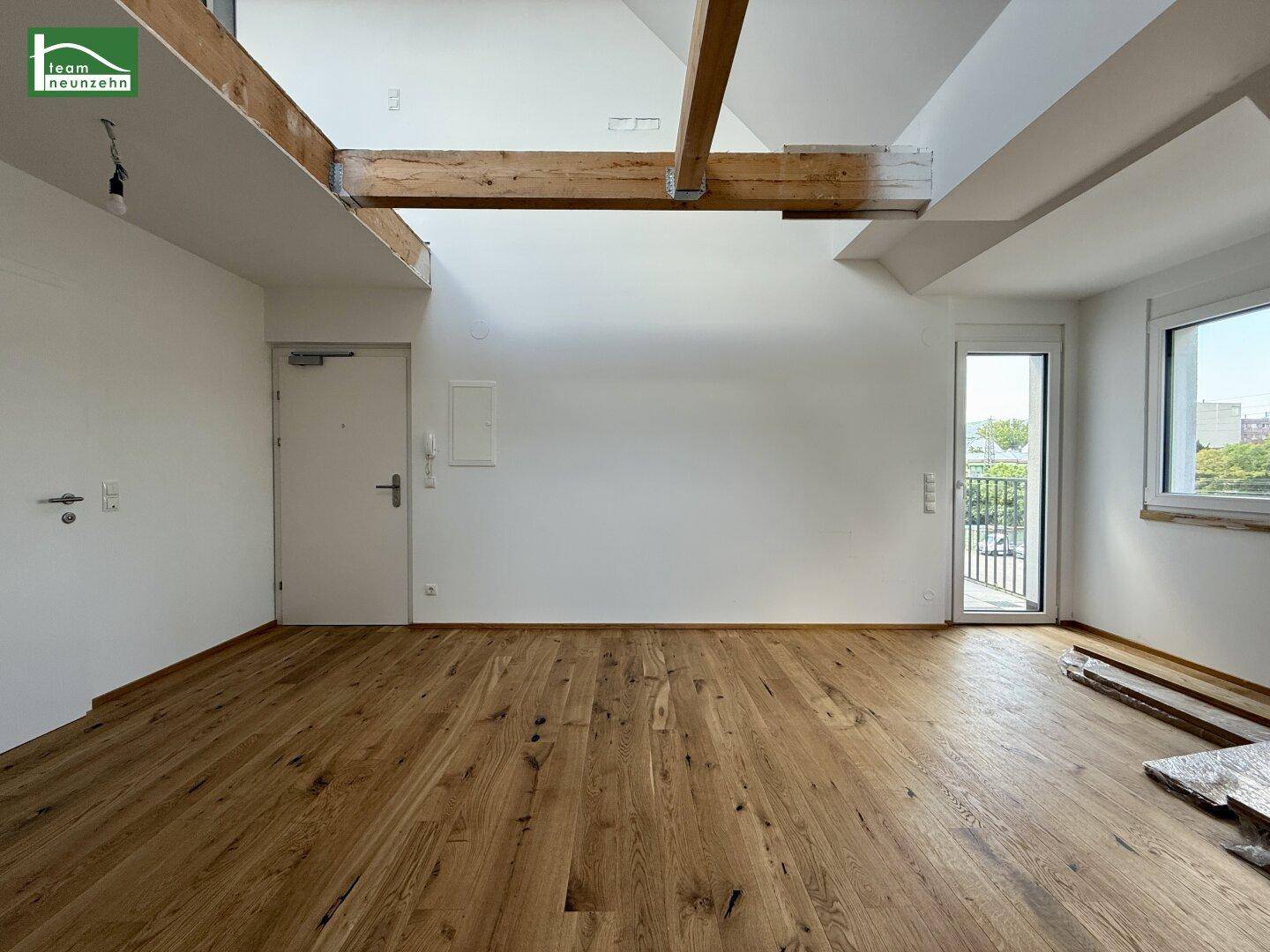 Heller Wohnbereich mit Holzboden, sichtbaren Holzbalken und Zugang zu einem französischen Balkon.