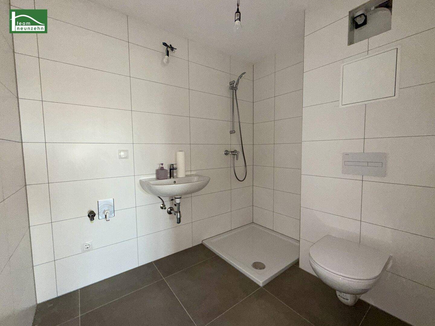 Modernes Badezimmer mit weißen Fliesen, Dusche, Waschbecken und wandhängendem WC.