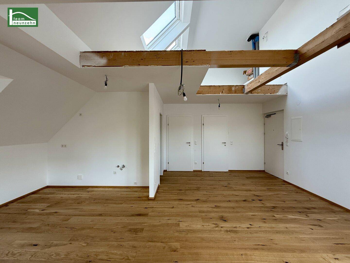 Offener Wohnbereich mit Holzboden, Dachfenster und sichtbaren Holzbalken, schafft ein loftartiges Gefühl.