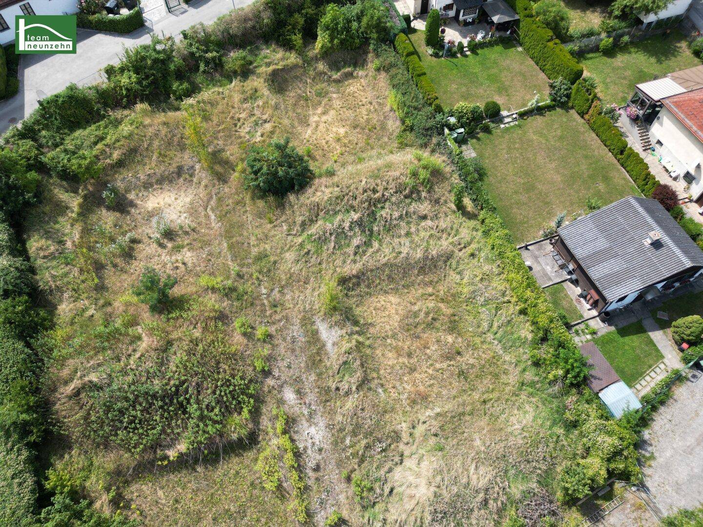 Luftaufnahme eines großen, unbebauten Grundstücks mit angrenzendem Garten und Wohnbebauung.