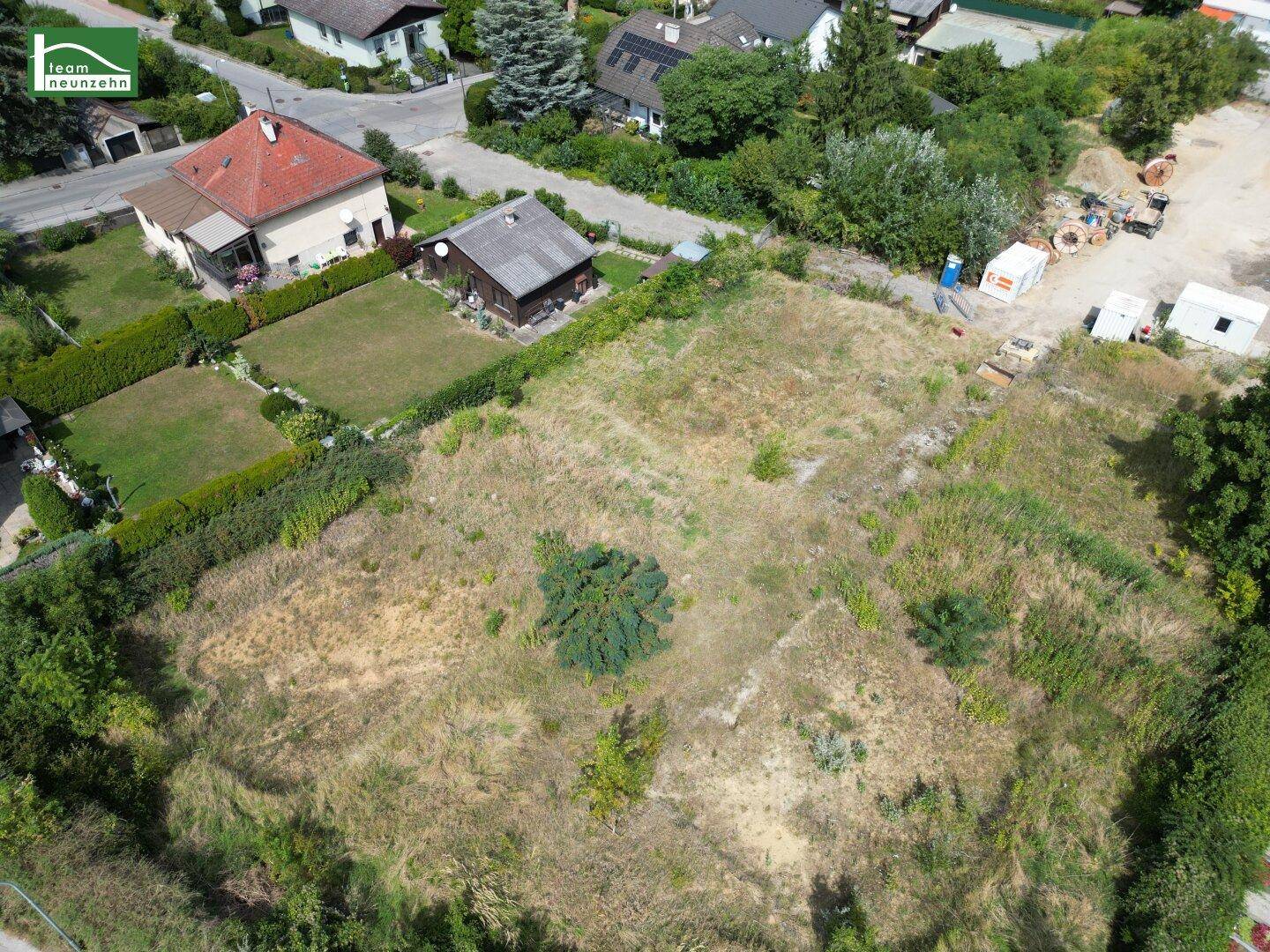 Luftaufnahme eines unbebauten Grundstücks mit umliegenden Wohnhäusern und viel Grün.