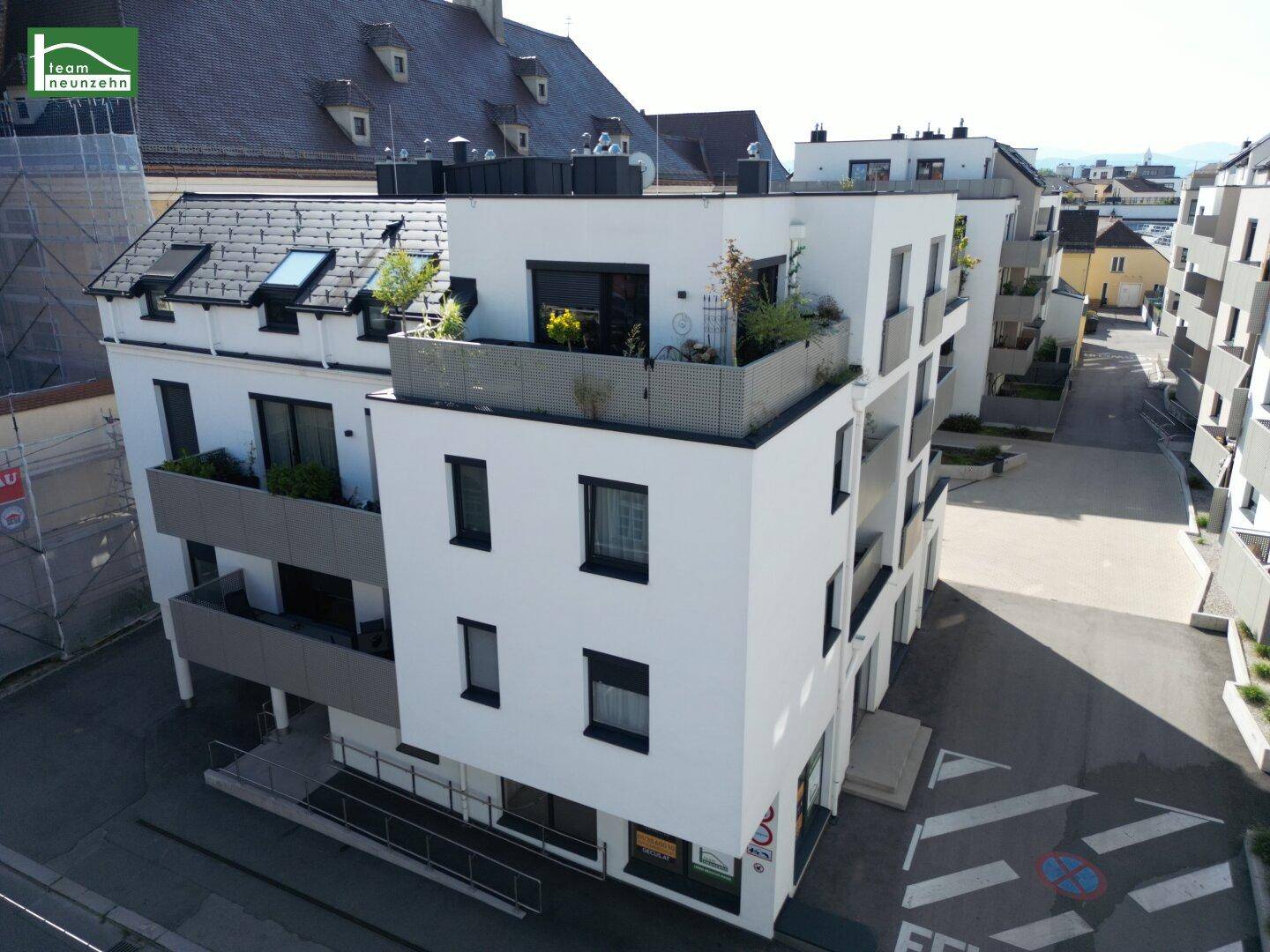 Moderne Wohnanlage mit weißer Fassade, Balkonen und Dachterrassen in städtischer Umgebung.