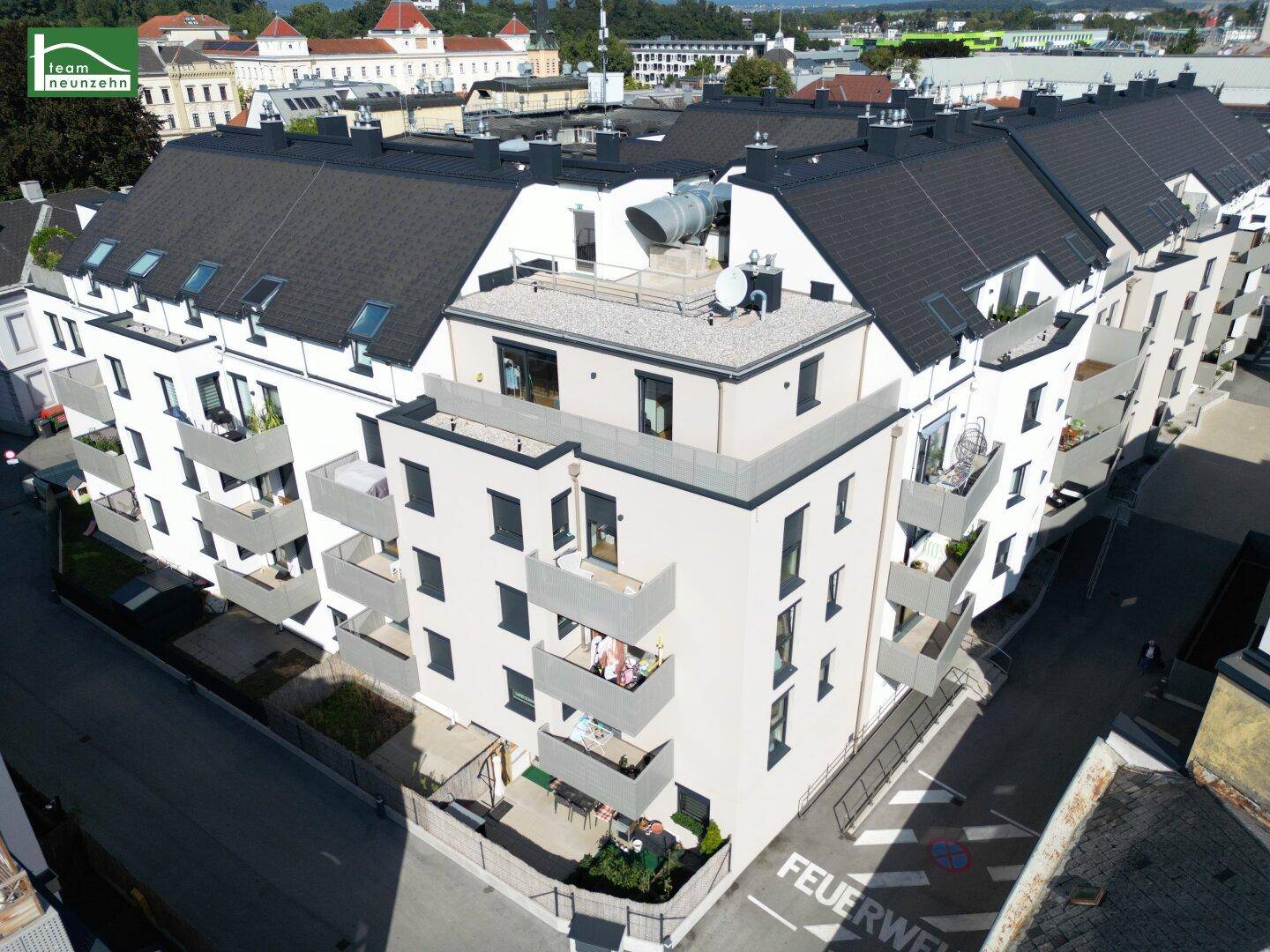 Luftaufnahme einer modernen Wohnanlage mit mehreren Balkonen und Schrägdächern in urbaner Lage.