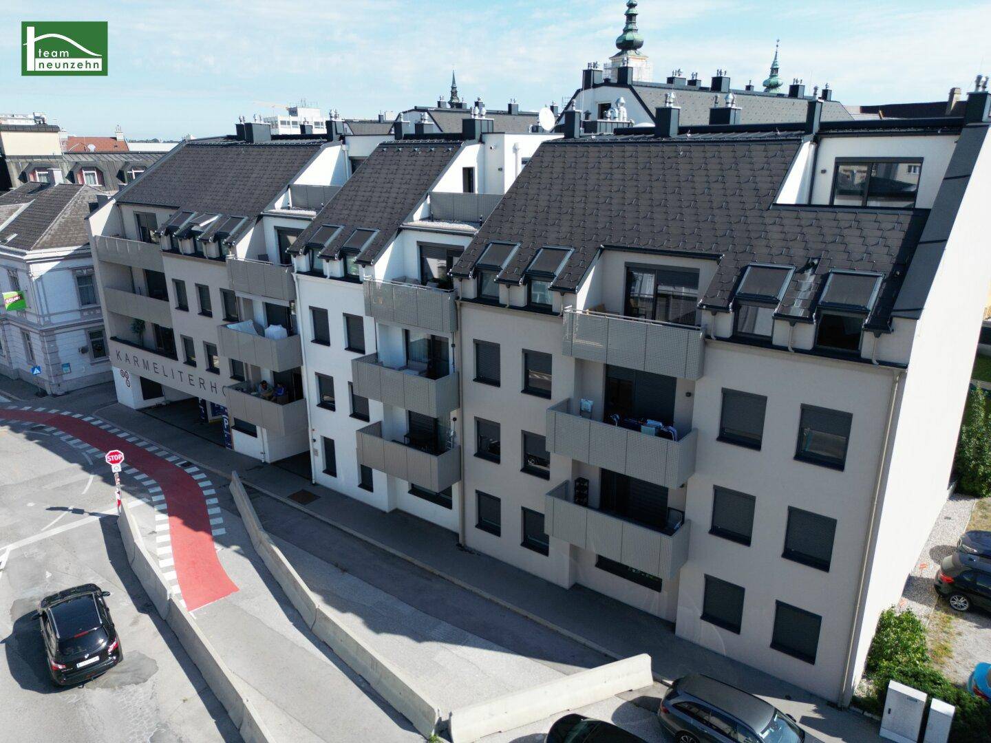 Lange Fassade einer modernen Wohnanlage mit Balkonen und Dachgauben entlang einer Straße.
