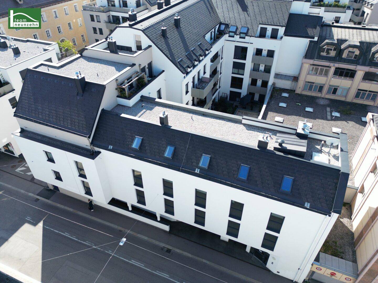 Ansicht einer modernen Wohnanlage mit Flachdach, Dachfenstern und weißer Fassade in der Stadt.