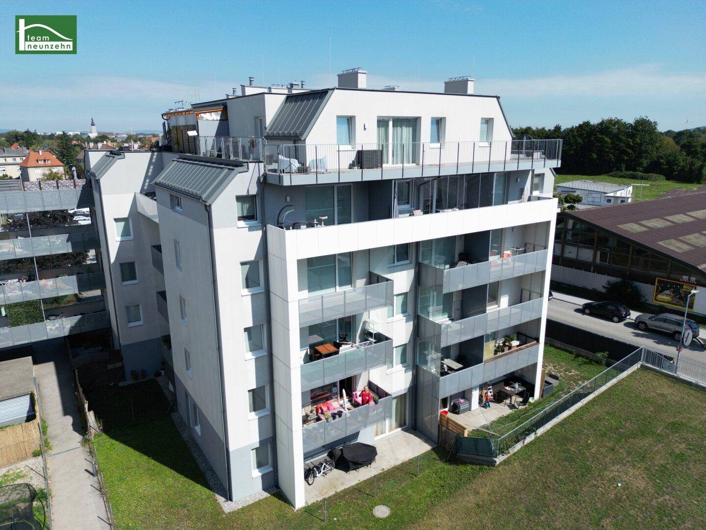 Nahaufnahme eines modernen Wohngebäudes mit mehreren Balkonen und einer Dachterrasse unter blauem Himmel.