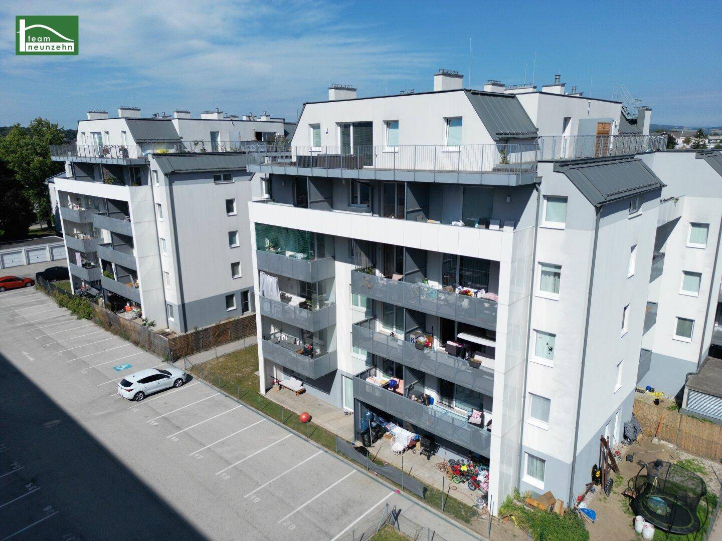 Ansicht eines modernen Wohnkomplexes mit Balkonen und einem großen Parkplatz im Vordergrund.