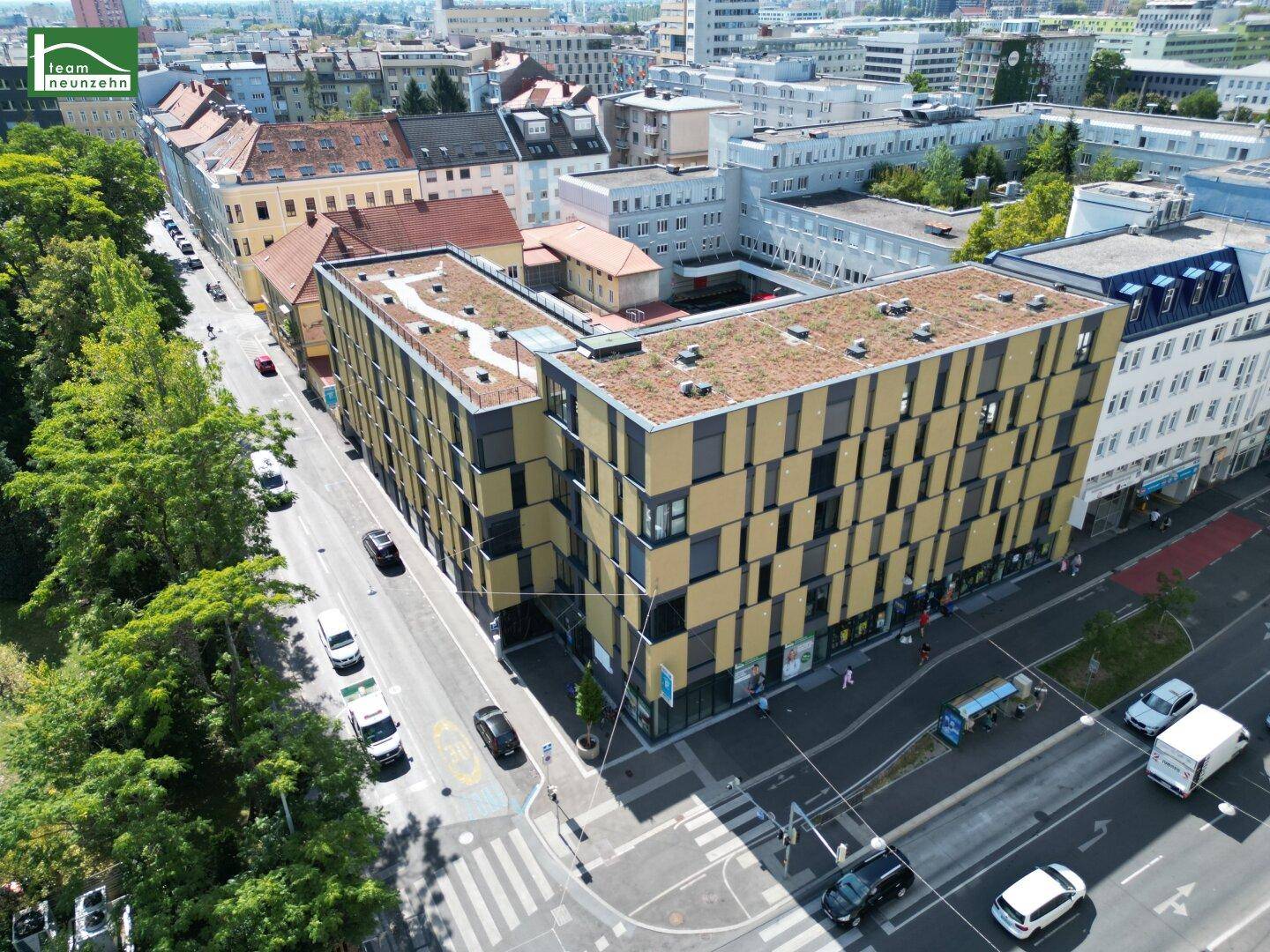 Luftaufnahme eines modernen Gebäudes mit begrüntem Flachdach in urbaner Umgebung mit viel Grün.