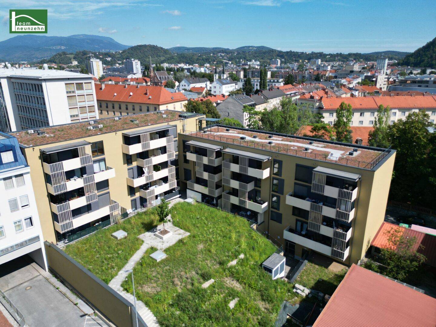 Rückseite eines modernen Wohngebäudes mit Balkonen und einer grünen Innenhof-Gartenanlage.