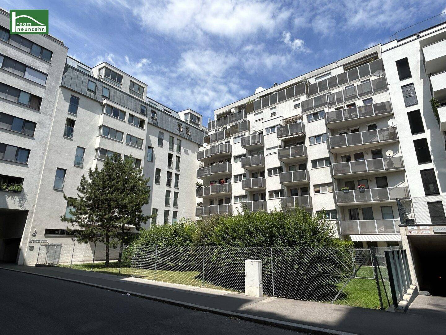 Moderne Wohngebäude mit Balkonen und einer kleinen Grünfläche davor unter blauem Himmel.