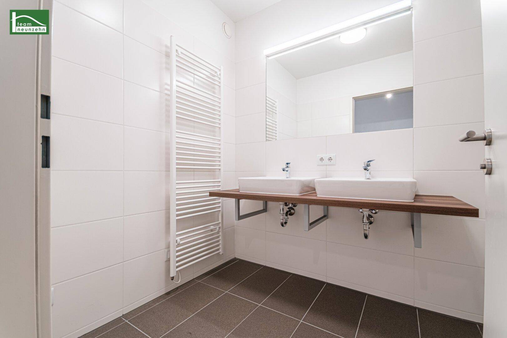 Modernes Badezimmer mit Doppelwaschbecken, beheiztem Handtuchhalter und weißen Fliesen.