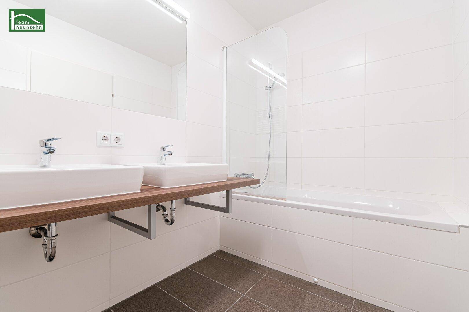 Helles Badezimmer mit Badewanne, Doppelwaschbecken und modernen Armaturen.