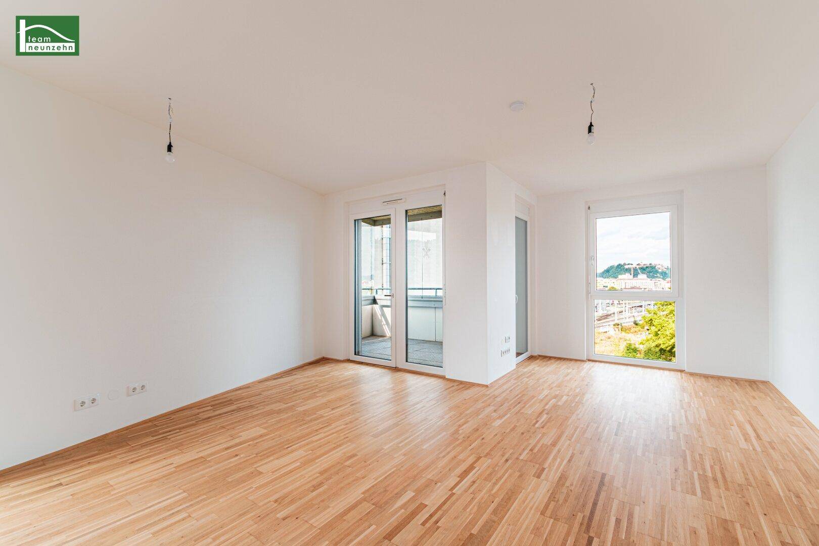Heller, leerer Raum mit Holzboden und Zugang zu einem Balkon, ideal als Wohnzimmer.