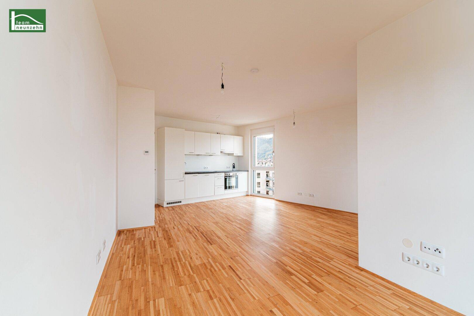 Geräumiger, leerer Wohn-Essbereich mit integrierter Küchenzeile und Holzboden.