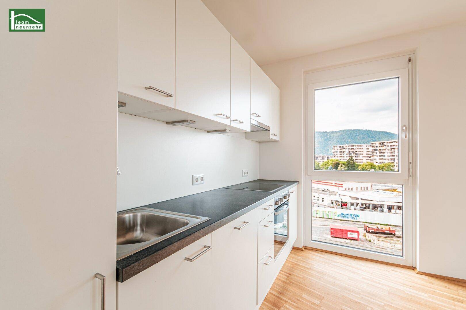 Moderne Küchenzeile mit weißen Schränken, dunkler Arbeitsplatte und Fensterblick.