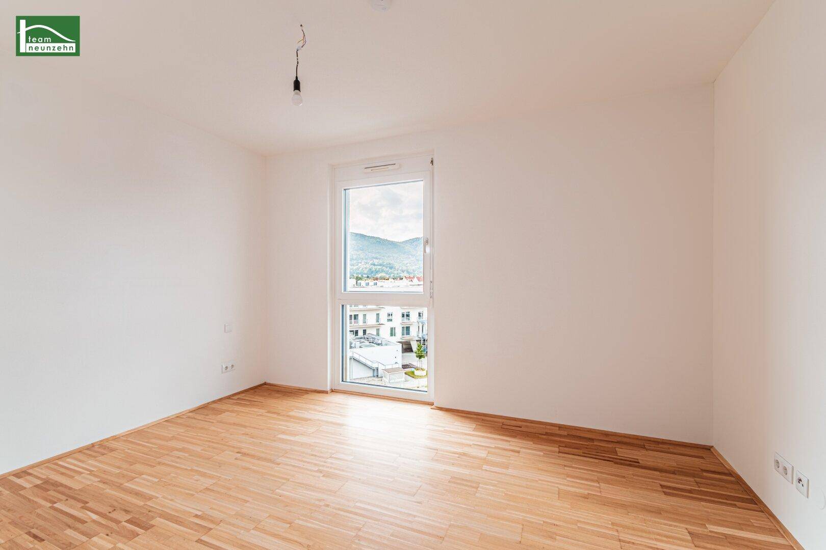 Leeres Schlafzimmer mit Holzboden und Fenster, das einen Blick auf die Umgebung bietet.