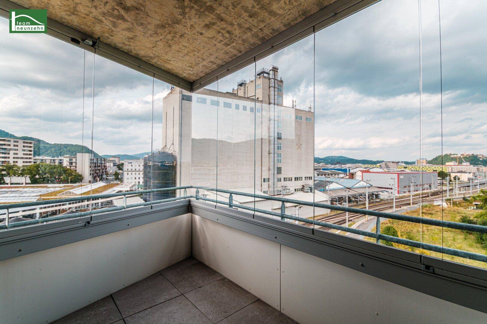 Verglaster Balkon mit Fliesenboden und weitem Blick über die Stadt und Bahnanlagen.