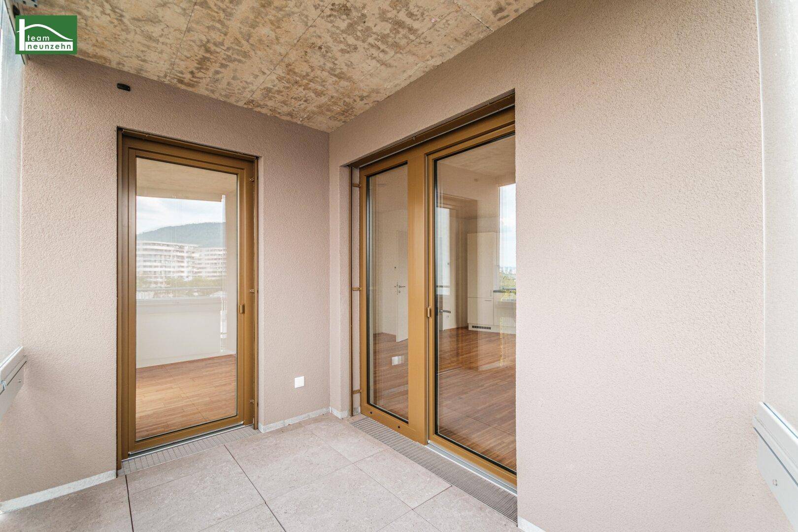Heller Balkon mit Fliesenboden und Zugang zum Innenraum durch große Glastüren.