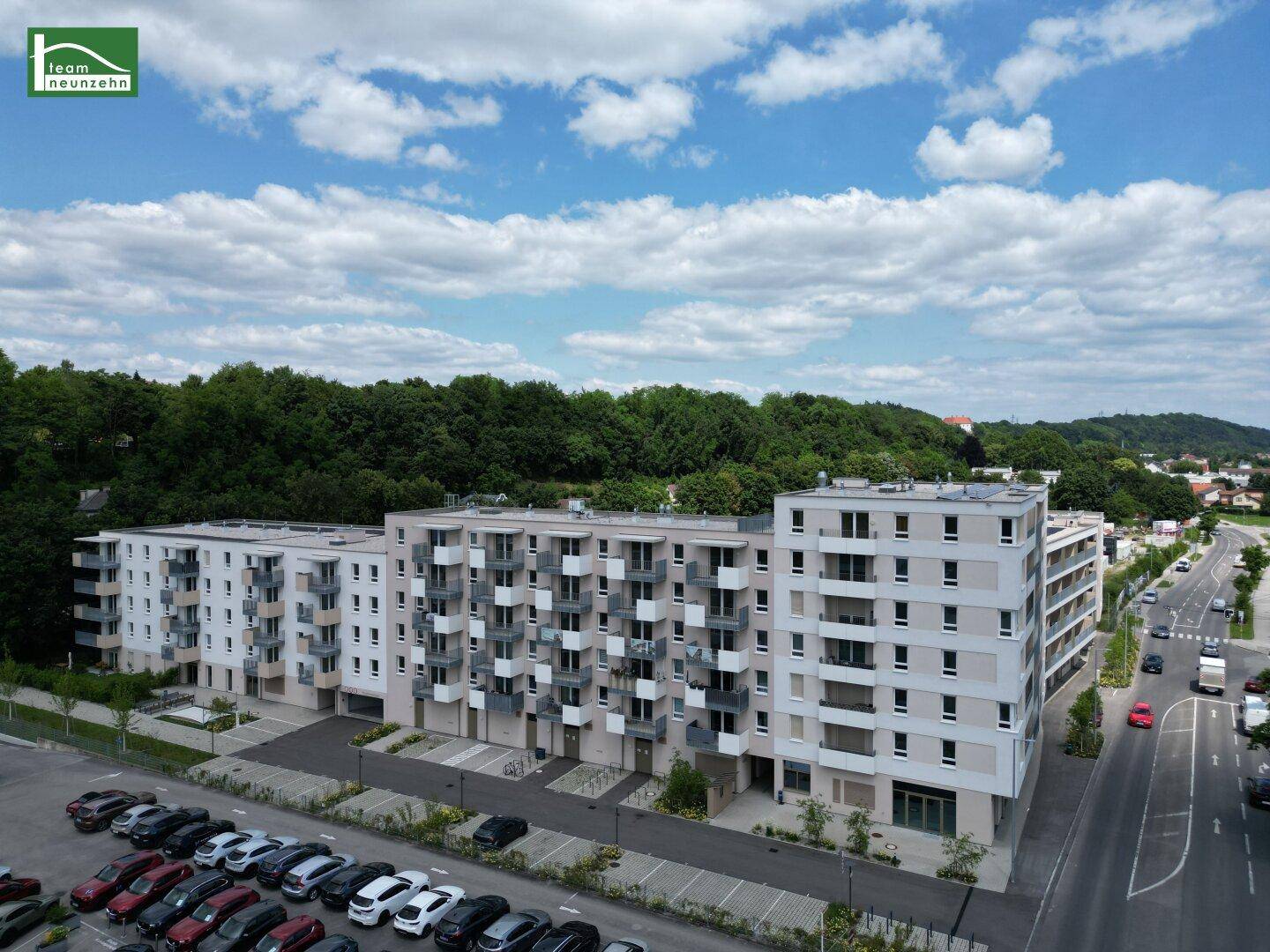 Weitläufige Luftaufnahme eines modernen Wohnkomplexes mit Balkonen, Parkplätzen und umgebender Natur.