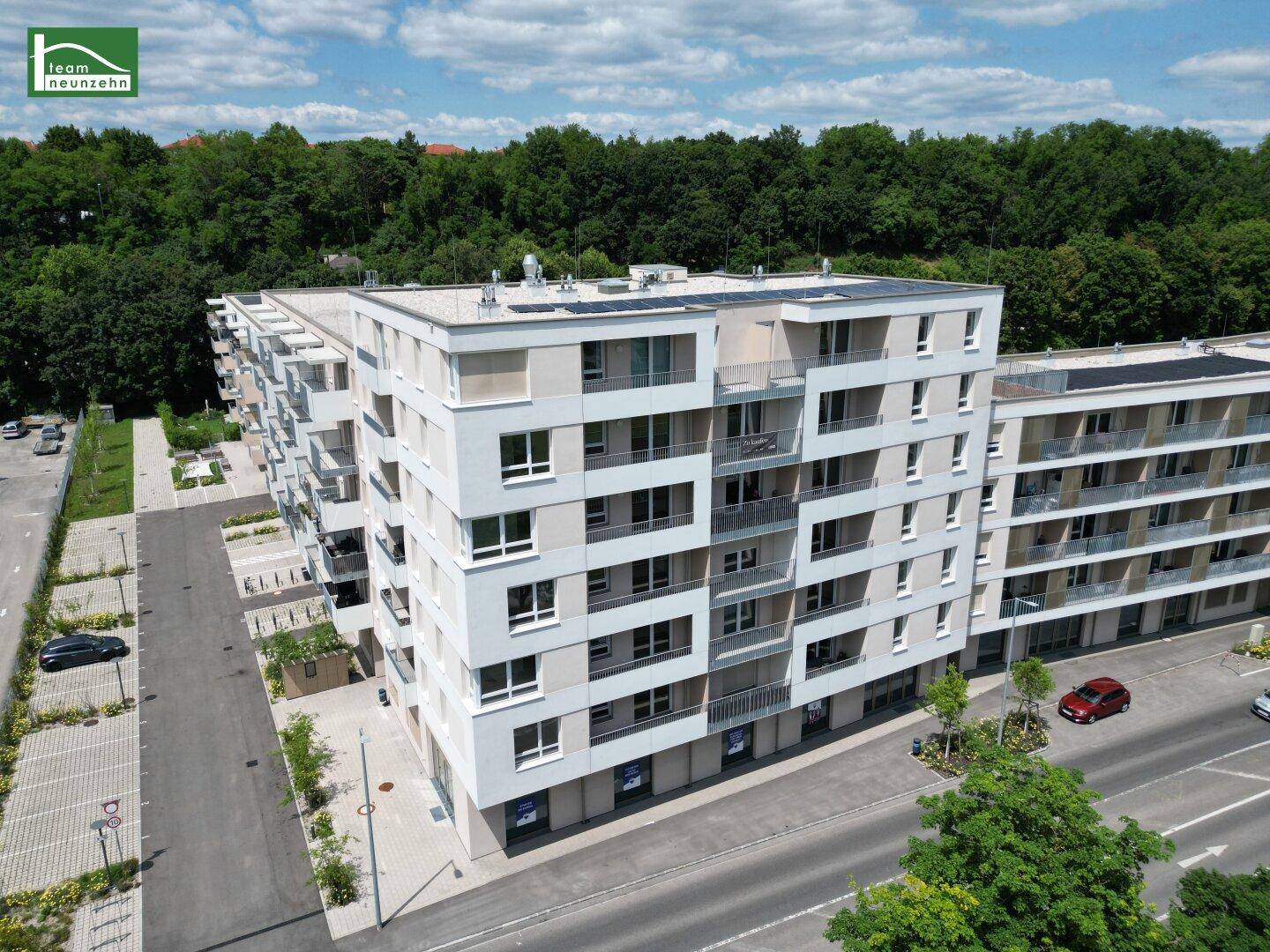 Moderner Wohnkomplex mit Balkonen und Flachdach, angrenzend an eine Straße und zahlreiche Parkplätze.
