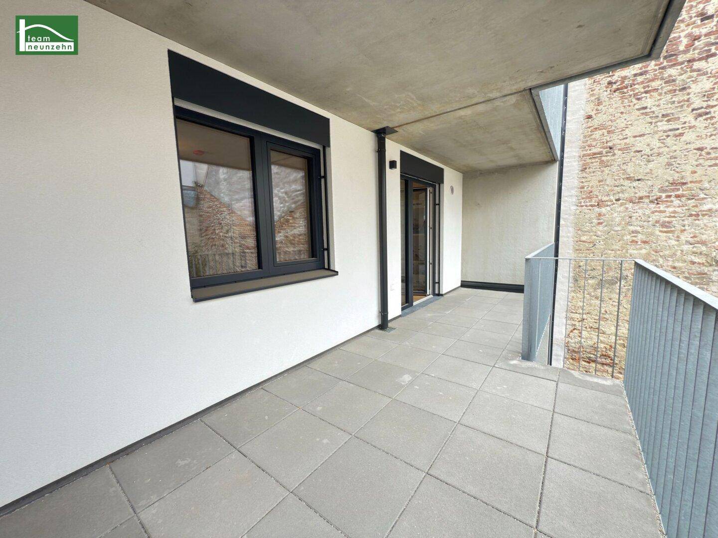 Heller Balkon mit Fliesenboden und Zugang zum Innenraum durch eine große Glastür.