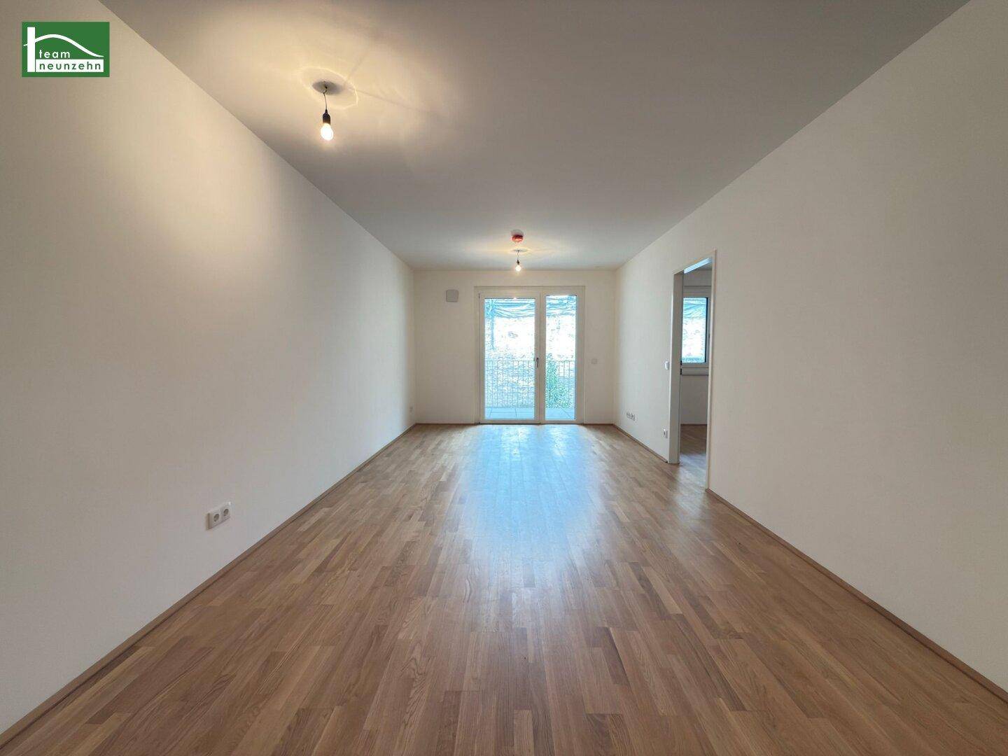 Geräumiger, leerer Wohnraum mit hellem Parkettboden und Zugang zu einem Außenbereich.