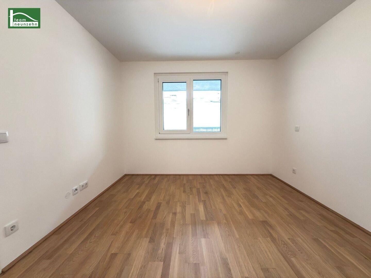 Helles Schlafzimmer mit Parkettboden und einem großen Fenster, bereit zur individuellen Gestaltung.