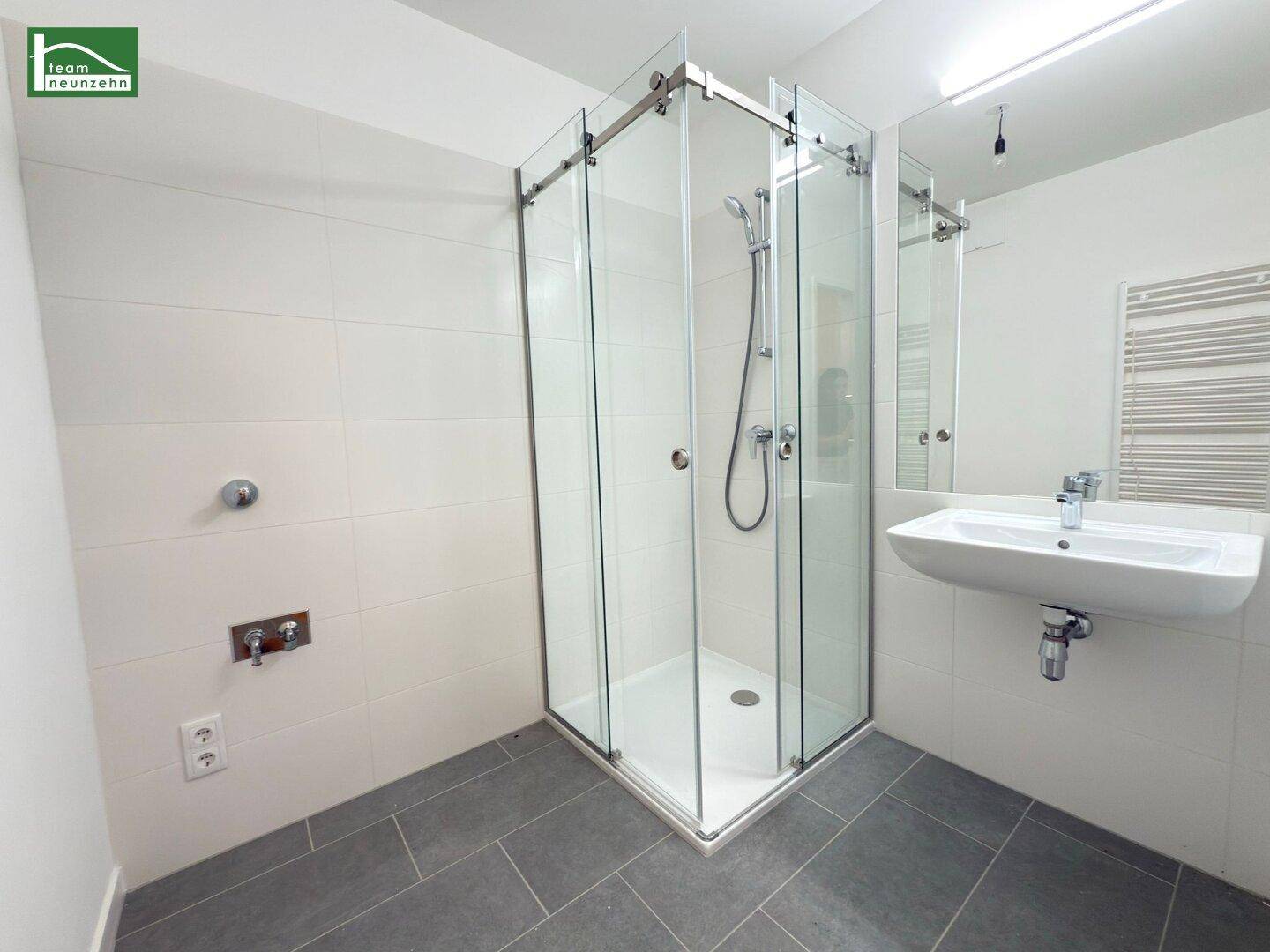 Modernes Badezimmer mit Duschkabine, Waschbecken und beheiztem Handtuchhalter.