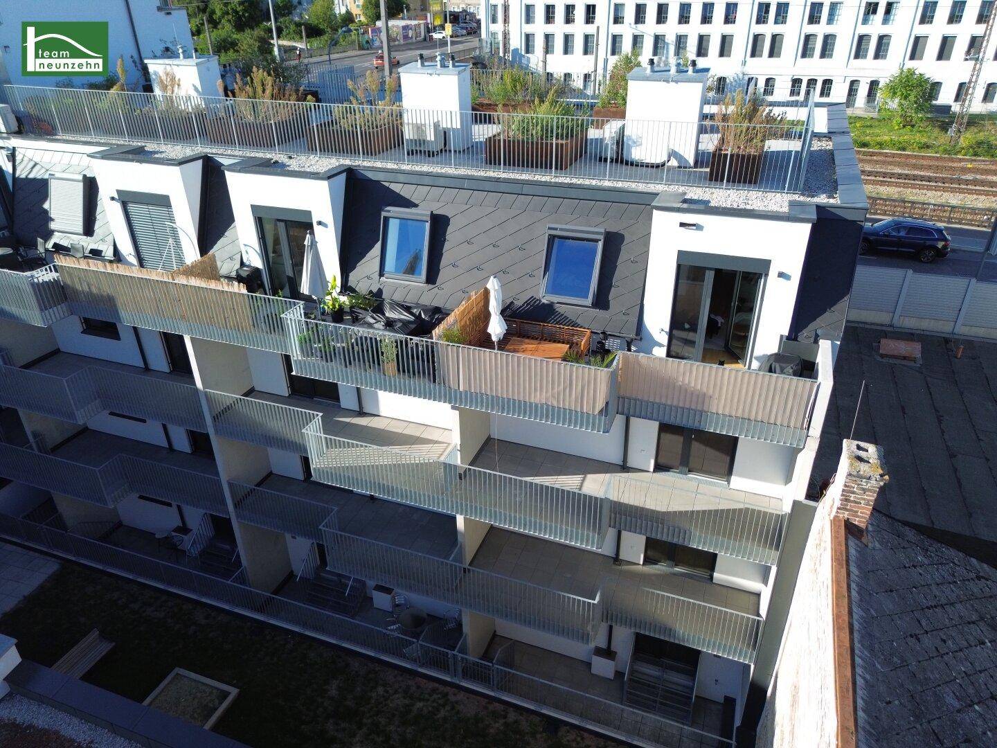 Dachansicht des Gebäudes mit mehreren Terrassen und Dachfenstern, umgeben von urbaner Bebauung.